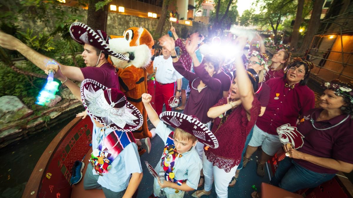 LeeRoy the Tiger, students, and staff ride a barge in the annual Fiesta River Parade